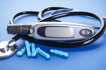 Digital glucometer and lancet pen and stethoscope on blue background, close-up. Diabetes concept,...