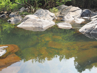 In the jungle, a clear river among huge boulders and stones.