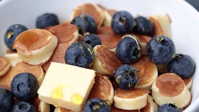 Pancake cereal with syrup, butter and berries in a white bowl, tiny pancakes