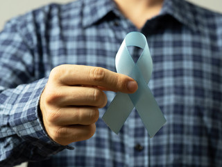 A man in a checked shirt holds a blue ribbon in his hand-a symbol of prostate cancer...