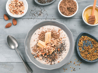 Overnight oats in bowl and ingredients - banana, LSA, chia seeds, almond, honey and pollen on gray wooden table background. Healthy breakfast oatmeal recipe idea. Top view