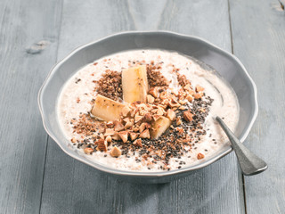 Close up view of overnight oats in bowl with banana, LSA, chia seeds, almond and honey on gray wooden table background. Healthy breakfast oatmeal recipe idea
