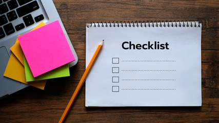 Notepad with a paper written Checklist on wooden office desk.