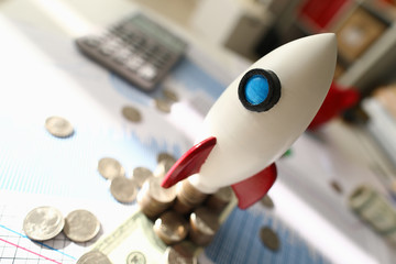 Space rocket model stands on document near coin