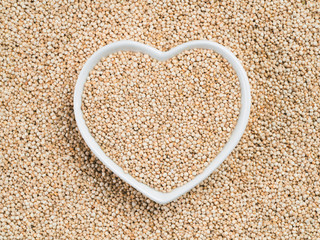 Quinoa in heart-shaped bowl on quinoa background. Gluten free ancient grain for healthy diet. I love quinoa concept. Copy space.
