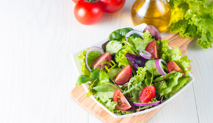 Fresh healthy vegetable salad made of cherry tomato, ruccola, feta, olives, cucumbers, onion and spices. Greek, Caesar salad in a white bowl on wooden background. Healthy organic diet food concept.