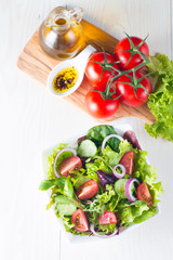 Fresh healthy vegetable salad made of cherry tomato, ruccola, feta, olives, cucumbers, onion and spices. Greek, Caesar salad in a white bowl on wooden background. Healthy organic diet food concept.