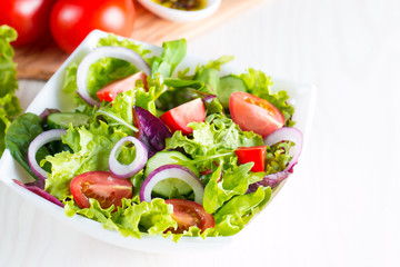 Fresh healthy vegetable salad made of cherry tomato, ruccola, feta, olives, cucumbers, onion and spices. Greek, Caesar salad in a white bowl on wooden background. Healthy organic diet food concept.