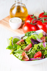 Fresh healthy vegetable salad made of cherry tomato, ruccola, feta, olives, cucumbers, onion and spices. Greek, Caesar salad in a white bowl on wooden background. Healthy organic diet food concept.