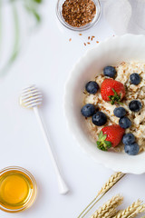 Oatmeal porridge with strawberry, blueberry, flax seeds and honey on white background.