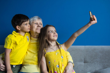 An old grandmother and her beloved grandchildren sit at home and take photos on their smartphone