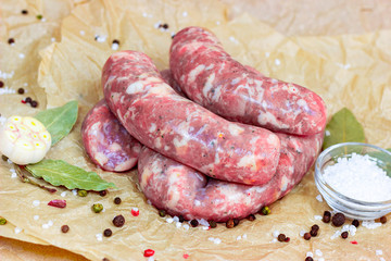 Fresh raw uncooked homemade pork sausages with garlic and spices on light wooden background in the kitchen.