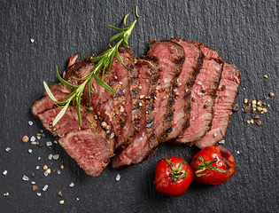 Grilled sliced beef steak with tomatoes on black background top view