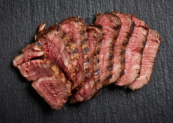 Sliced grilled beef steak on black background top view