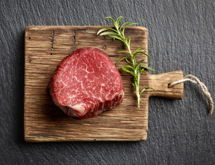 Raw beef fillet steaks on wooden board and black background top view