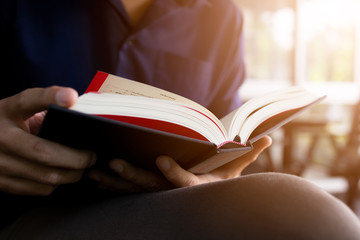 young man is sitting reading in the window in the room with soft-focus and over light in the background