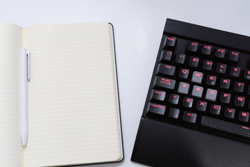 Pen on a notebook next to a computer keyboard on a white background