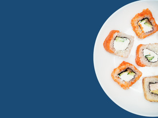 Sushi rolls on a round white plate on a blue background. Copyspace.
