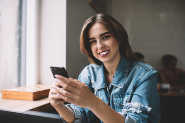 Cheerful woman browsing smartphone in cafe