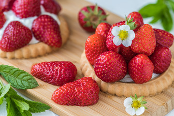 Strawberry tartlets on wooden board, decorated with blossoms, strawberries and mint leaves. Closeup.