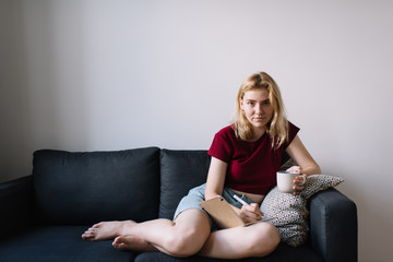 Obraz premium Young woman with cup of drink writing notes
