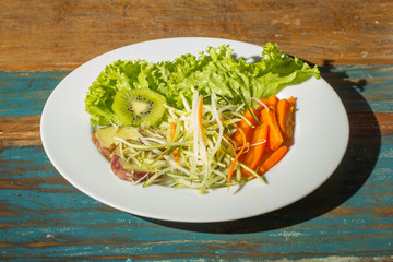 Food plate of salad. dish showing carrots, lettuce, kiwi. On rustic wooden table.