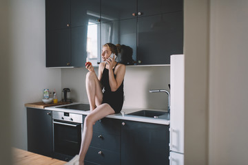 Positive woman talking on phone at kitchen