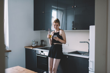 Cheerful female drinking fresh beverage and browsing mobile phone