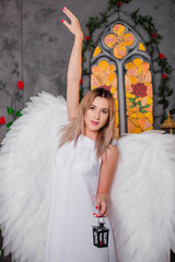 An angel in a white dress with wings spread wide behind poses with a lamp in his hands.