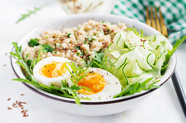 Breakfast oatmeal porridge with green herbs, boiled egg, cucumber and flax seeds. Healthy balanced food.