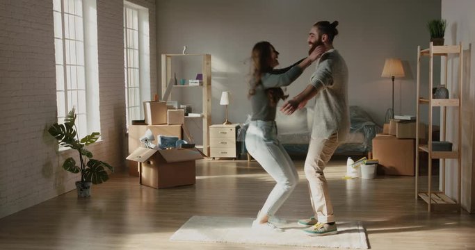 Happy caucasian newlyweds are enjoying thie new house, hugging and spinning around the room and positively smiling - new life, young family concept 4k footage