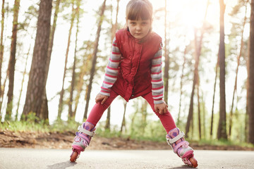 Outside picture of energetic serious little girl being in forest, having roller blades on legs,...