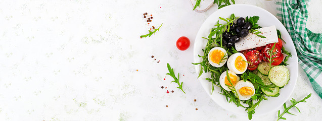 Breakfast. Greek salad and boiled eggs.  Fresh vegetable salad with tomato,  cucumbers, olives, arugula and feta cheese. Trend food. Top view, banner