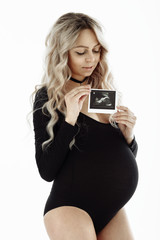 Beautiful pregnant happy women in black bodysuit isolated on gray background. Pregnant girl holding ultrasound