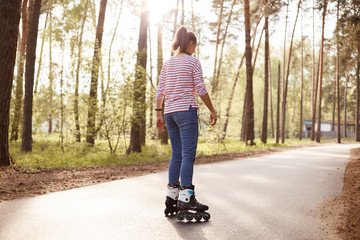 Back view of energetic slender young woman being in middle of road, wearing striped sweatshirt and...