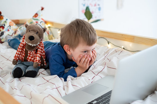 little boy lying in bed in nursery room watching at laptop, distant education, learning new, video chat, watching cartoons, spend time at home. Stay home.