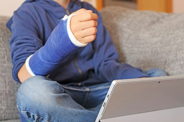 Junge mit Gipsarm sitzt mit dem Tablet auf dem Sofa (Model released)