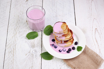 Tasty beautiful pancakes in a white plate with cherry and yogurt in a glass cup on a light wooden background with mint leaves. The concept of a healthy diet and a great breakfast