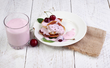 Tasty beautiful pancakes in a white plate with cherry and yogurt in a glass cup on a light wooden background with mint leaves. The concept of a healthy diet and a great breakfast