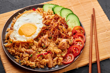 Nasi Goreng - Indonesian Chicken Fried Rice on a black plate on dark slate backdrop. Nasi Goreng is an Indonesian cuisine dish with jasmine rice, chicken meat, fried onion, egg and vegetables