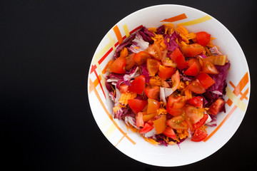 Salad with carrots and tomatoes on black table, top view