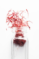 Saffron in a glass jar is scattered on white..Spicy seasoning top view.
