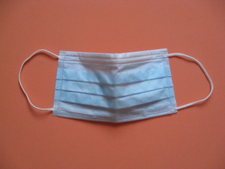 Mascarilla sanitaria quir&uacute;rgica azul ligeramente abierta sobre fondo naranja. Material sanitario para m&eacute;dicos y doctoras, enfermer@s, medidas higiene y sgeuridad