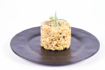 Risotto with button mushroom and bacon decorated with rosemary twig on a black plate on a white background