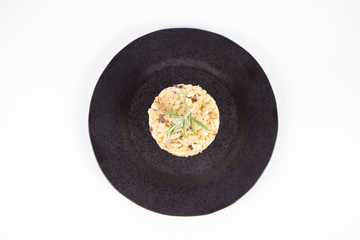 Risotto with button mushroom and bacon decorated with rosemary twig on a black plate on a white background