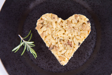 Heart shaped portion of Risotto with button mushroom and bacon decorated with rosemary twig on a black plate on a white background