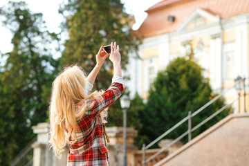 Stylish hipster girl using smartphone camera taking picture of architecture during sightseeing tour. Summer vacation.