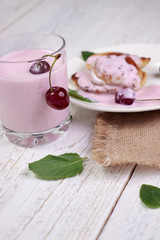Tasty beautiful pancakes in a white plate with cherry and yogurt in a glass cup on a light wooden background with mint leaves. The concept of a healthy diet and a great breakfast