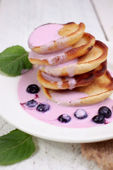 Tasty beautiful pancakes with blueberries and blueberry yogurt in a glass cup on a light wooden background with mint leaves. The concept of a healthy diet and a great breakfast