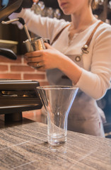 Making Latte - a large transparent glass for Latte. In the background is a girl at a coffee machine.